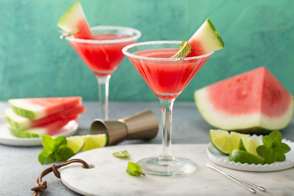Two Watermelon Martinis served in a martini glass and decorated with a piece of watermelon and sugar on the rim .
