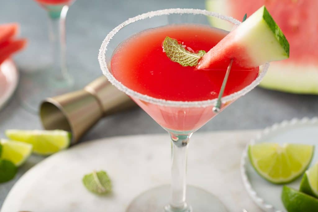 Close up view of a Watermelon Martini served in a martini glass and decorated with a piece of watermelon, sugar on the rim and a mint leaf.