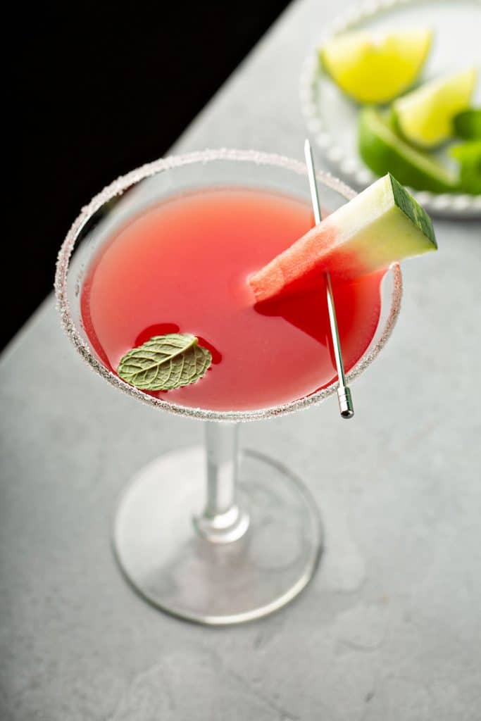 Top view of a Watermelon Martini served in a martini glass and decorated with a piece of watermelon, sugar on the rim and a mint leaf.