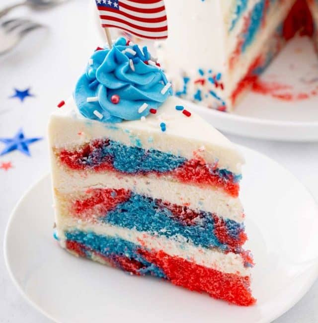 Slice of tie-dye red, white and blue frosted cake with an United States flag on top