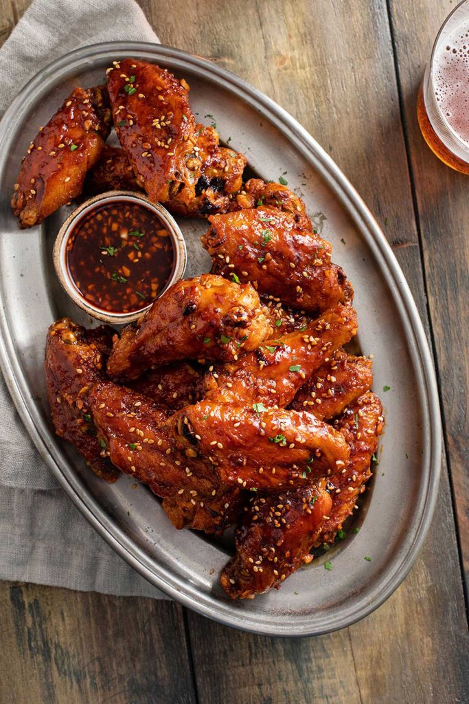 Crispy and caramelized korean chicken wings with sauce on a platter.
