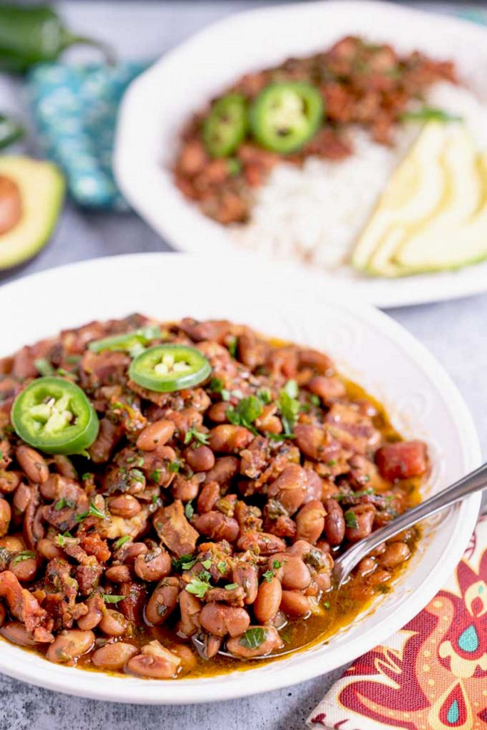 Charro beans in a white bowl topped with jalapeño peppers