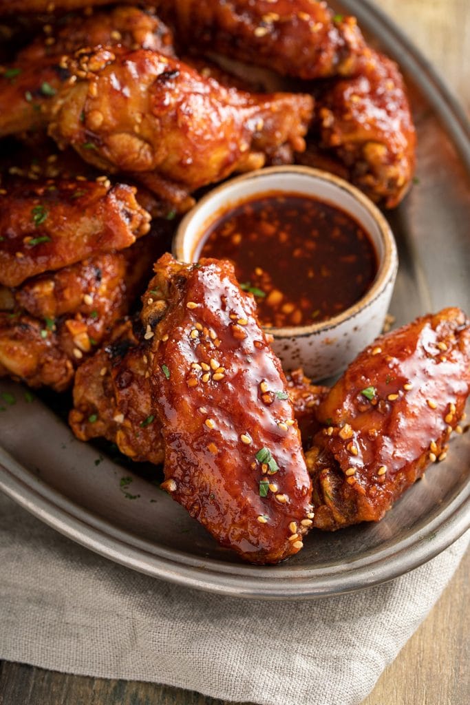 Crispy chicken wings smothered in a sweet and spicy Korean sauce on a plate.