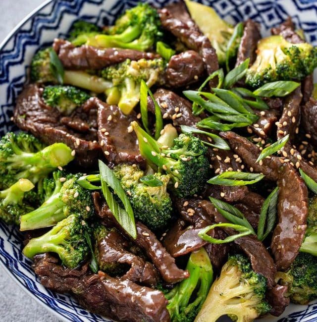 Close-up view of a bowl with beef and broccoli, garnished with sesame seeds and chopped green onion.