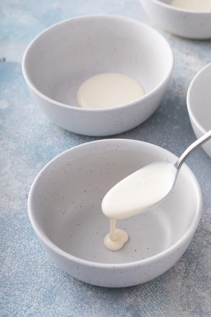 Pouring some cream at the bottom of a serving bowl, with a spoon.