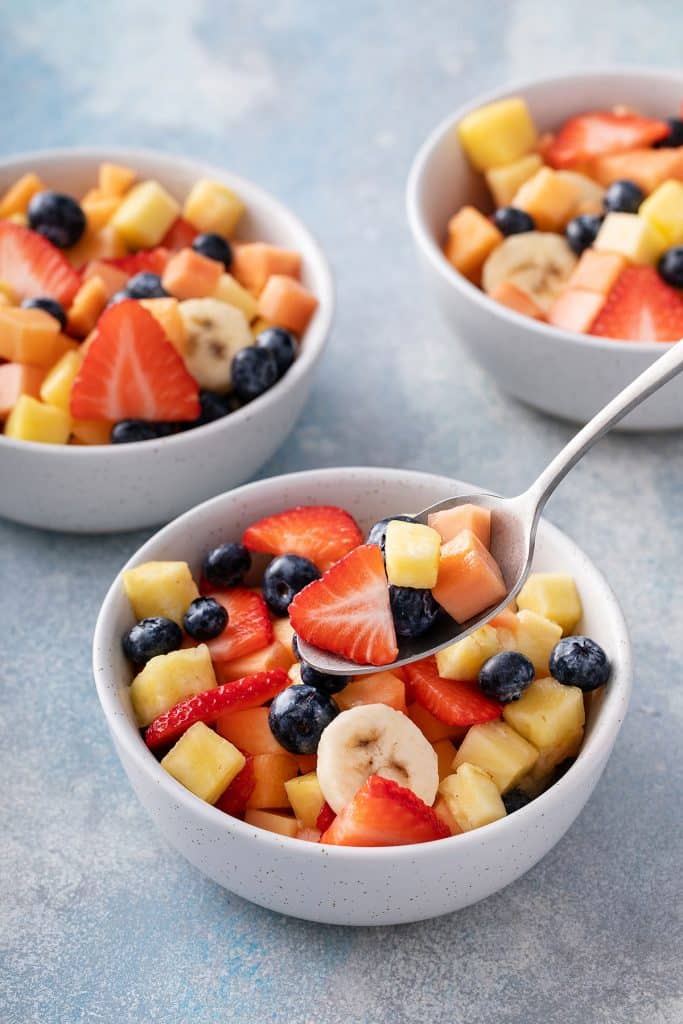Pouring chopped fruit over the cream in the same serving bowl.