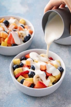 Smooth and luscious sweet creamy sauce is poured over a bowl of chopped fresh fruit.