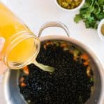 Adding broth to the pan with black beans and veggies