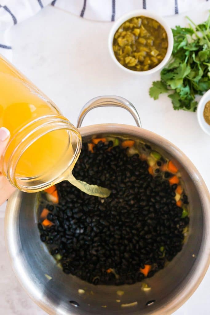 Adding broth to the pan with black beans and veggies