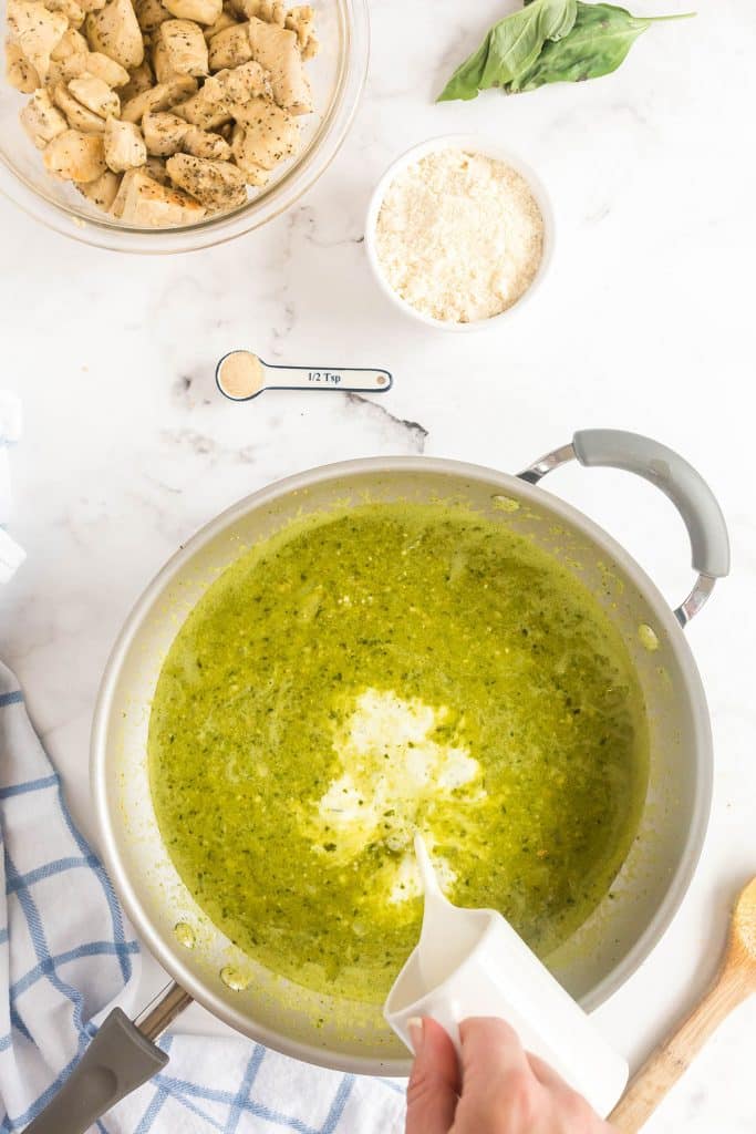 pouring half and half over the pesto sauce