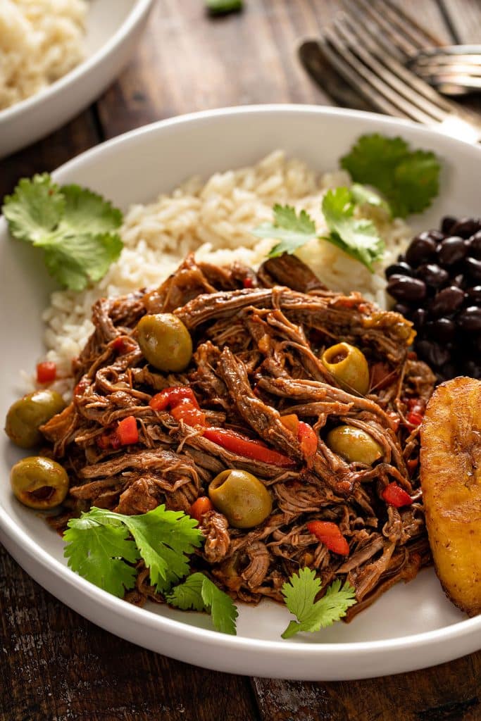 Shredded beef, bell peppers and olives Cuban Ropa Vieja served with rice, black beans and fried plantains.