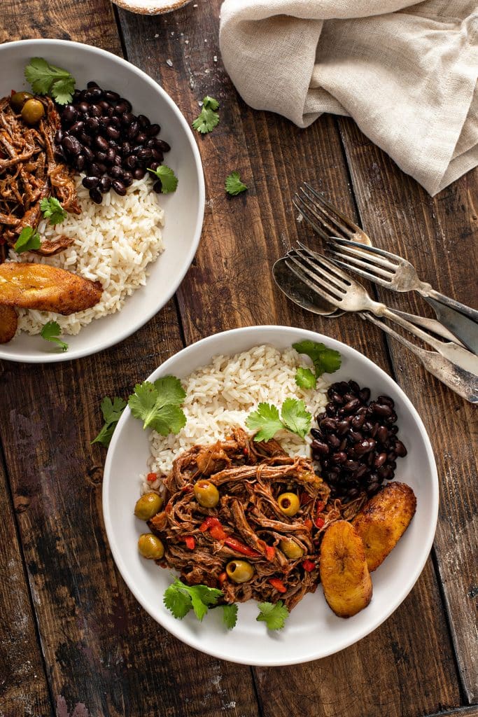 Bowls of ropa vieja with rice, beans and fried platanos maduros.