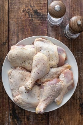 Chicken legs and thighs seasoned with salt and black pepper on a white plate