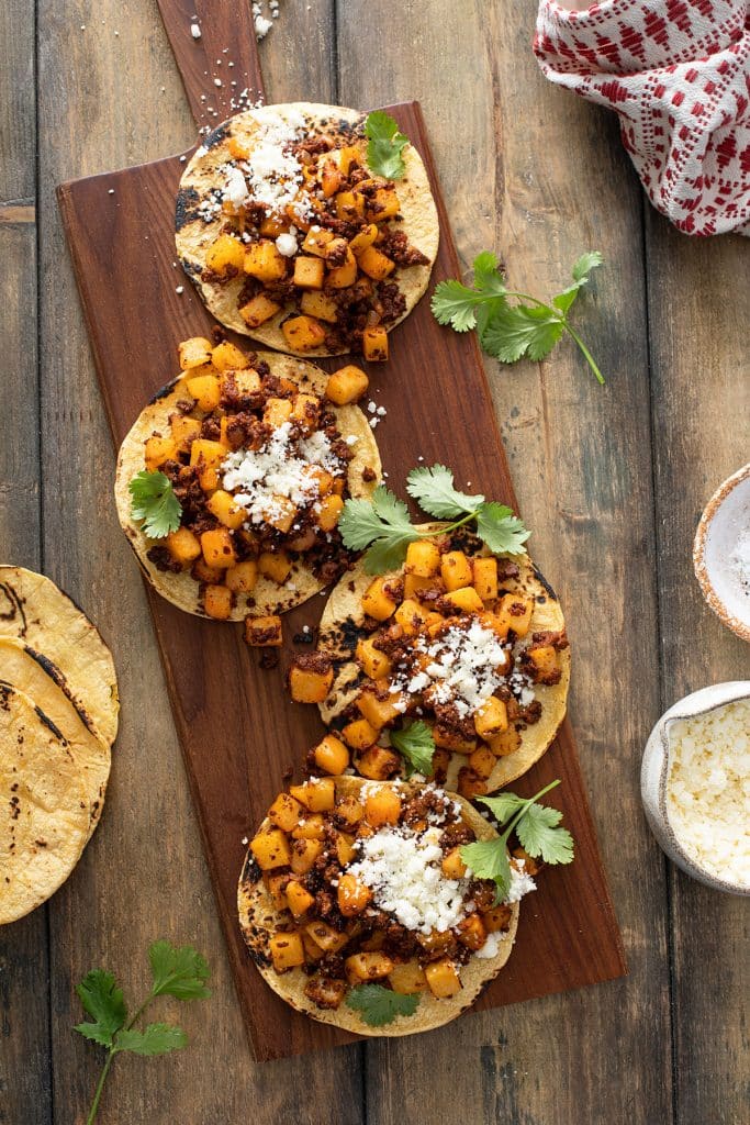 Papas con chorizo tacos made with corn tortillas and topped with cilantro and crumbled cheese on a wooden board.