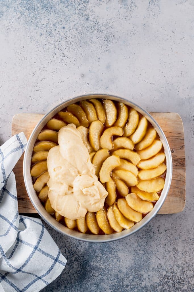 Scooping cake batter over caramelized apples on a pan