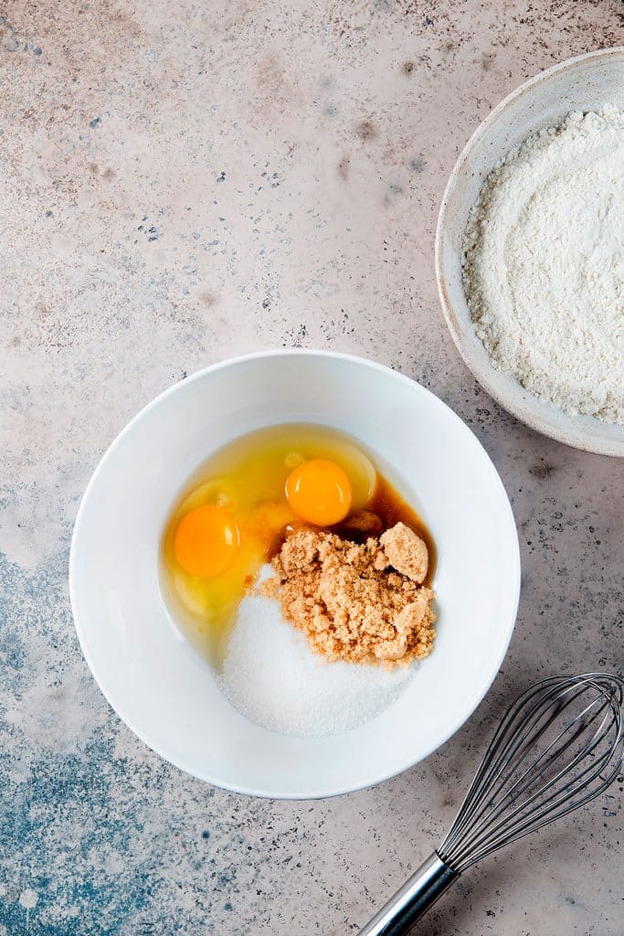 Brown sugar, granulated sugar and eggs in a white bowl.