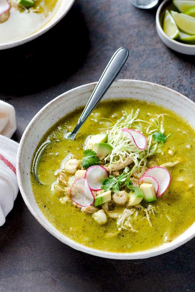 Big bowl of green pozole with hominy and toppings.