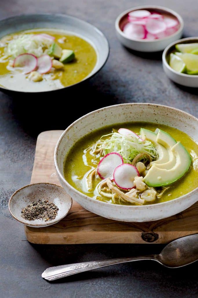 Bowl of pozole topped with avocado, radishes and cabbage