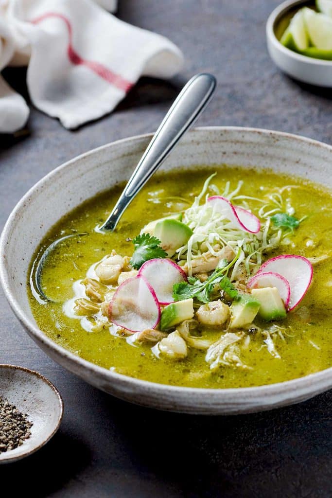 A bowl filled with chicken pozole verde and topped with shredded cabbage, radishes and cilantro