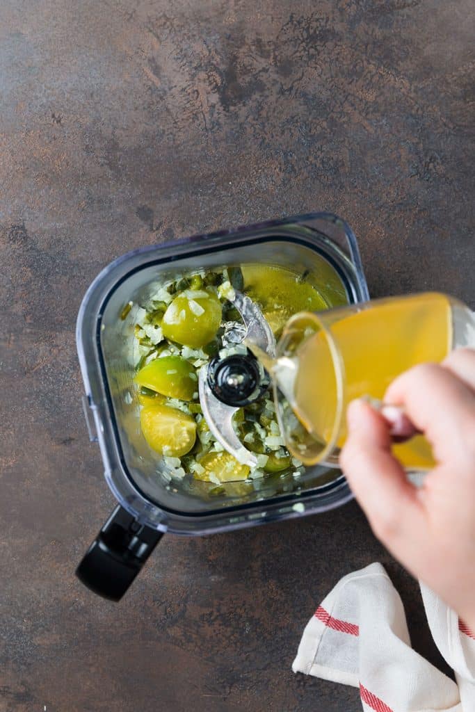 adding chicken broth into the blender with the tomatillos and the green chile mixture