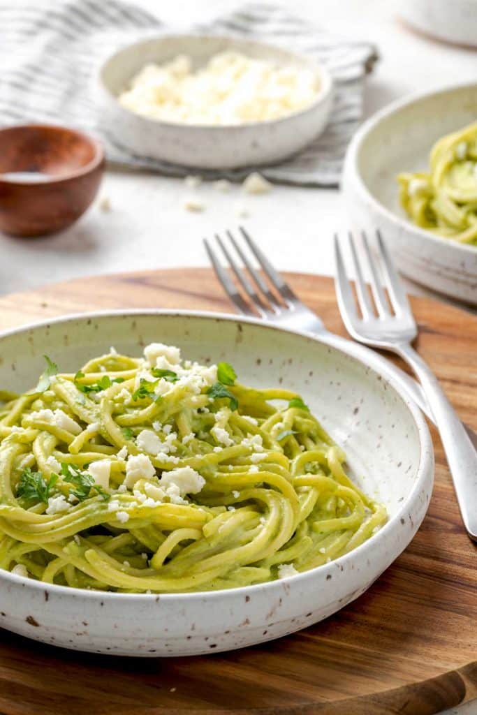 A bowl of rich and creamy roasted poblano and cilantro green sauce tossed with spaghetti noodles and topped with crumbled cheese.