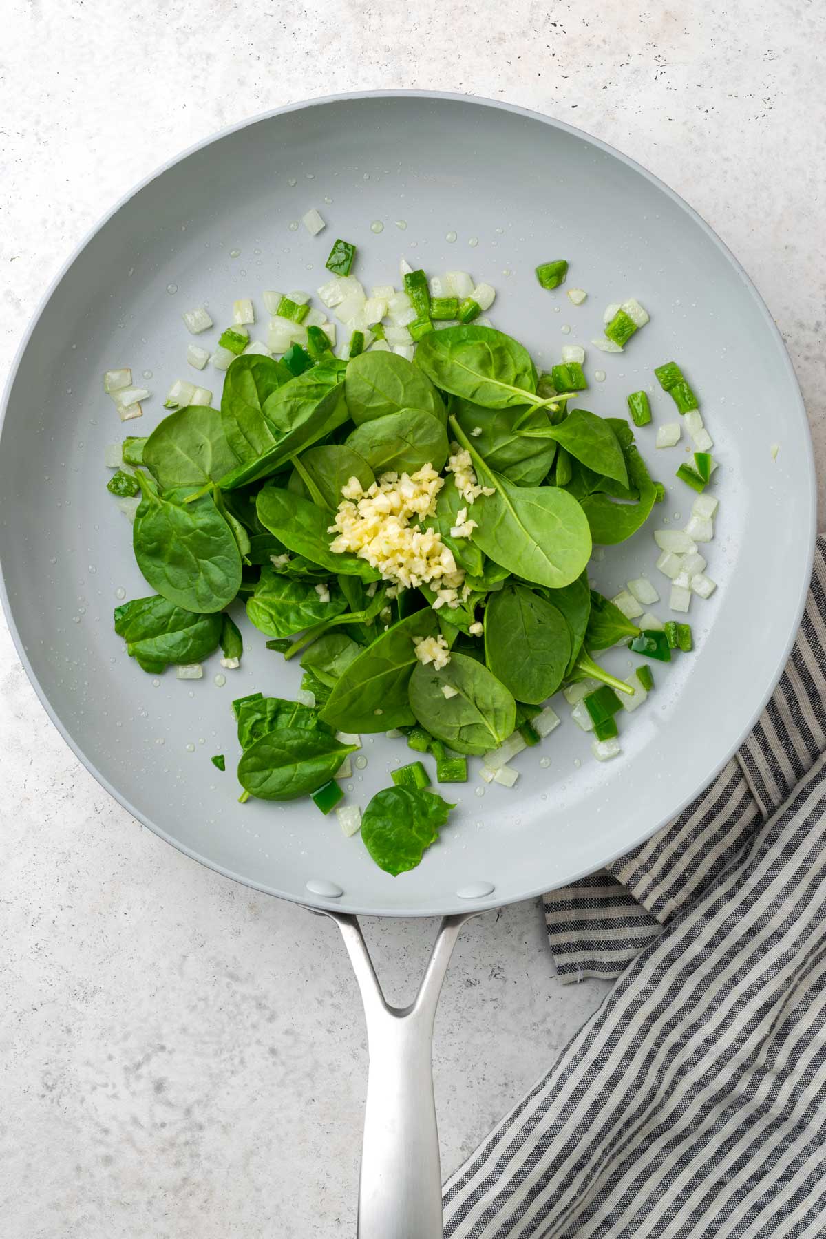 Sautéed onion and jalapeno pepper with baby spinach and garlic in a skillet