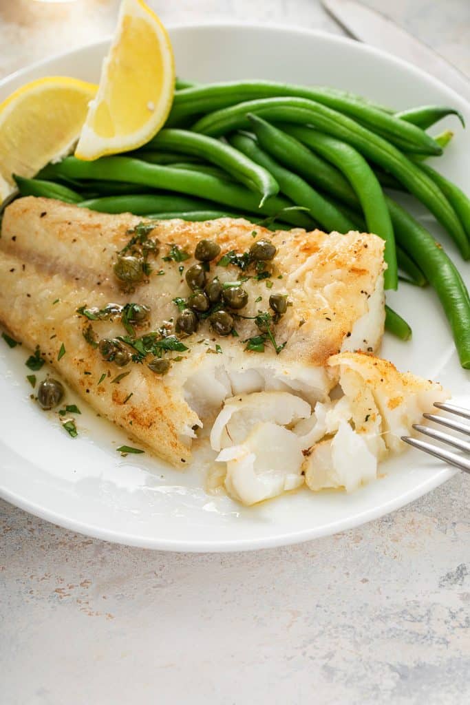 Lightly golden and flaky fish fillet on a plate topped with lemon butter and capers.