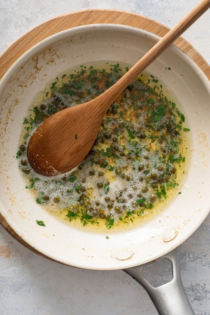 A skillet with lemon butter and capers pan sauce.