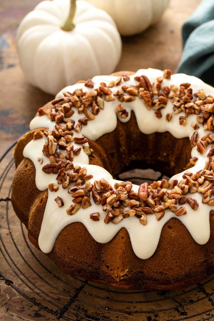Pumpkin bundt cake topped with cream cheese frosting and chopped pecans on a rack.