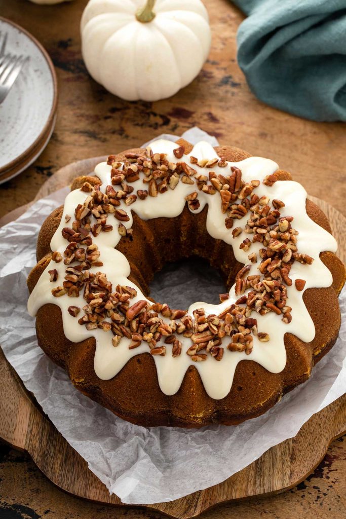 Pumpkin bundt cake topped with cream cheese frosting and chopped pecans.