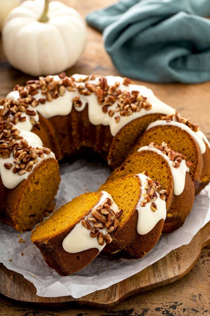 Sliced pumpkin bundt cake topped with cream cheese and pecans. 