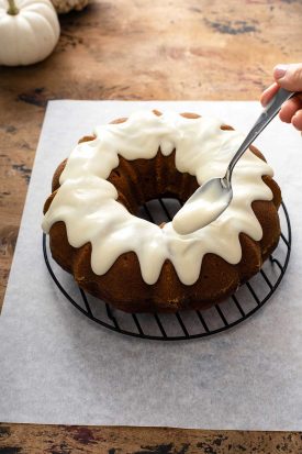 Pouring cream cheese frosting over pumpkin bundt cake with a spoon