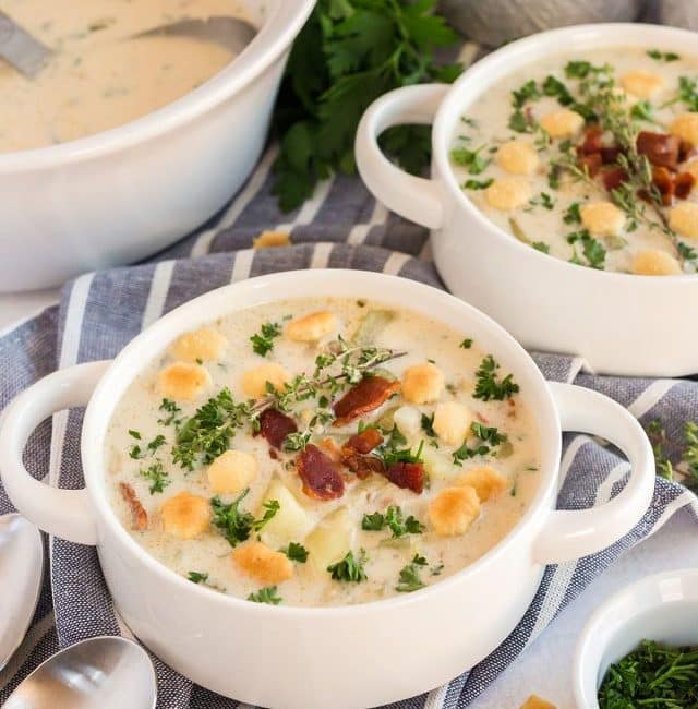Creamy clam chowder topped with bacon an oyster crackers serve in white bowls