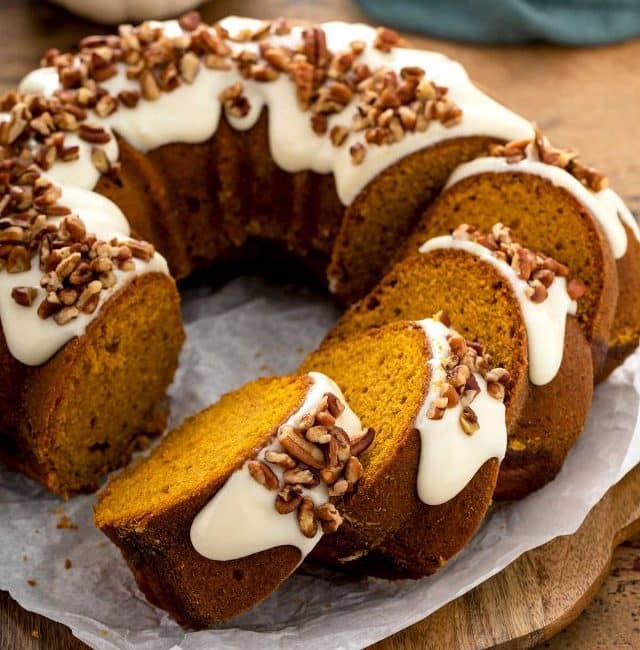 A sliced pumpkin bundt cake topped with cream cheese and pecans.