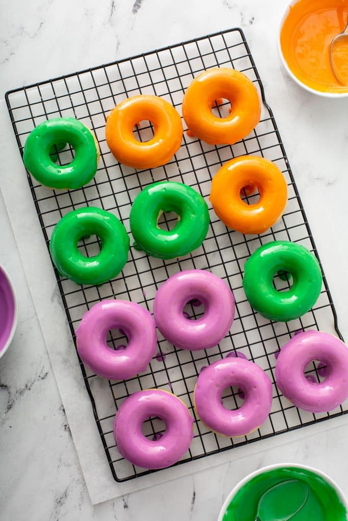 top view of 12 colorful glazed donuts drying on a cooling rack