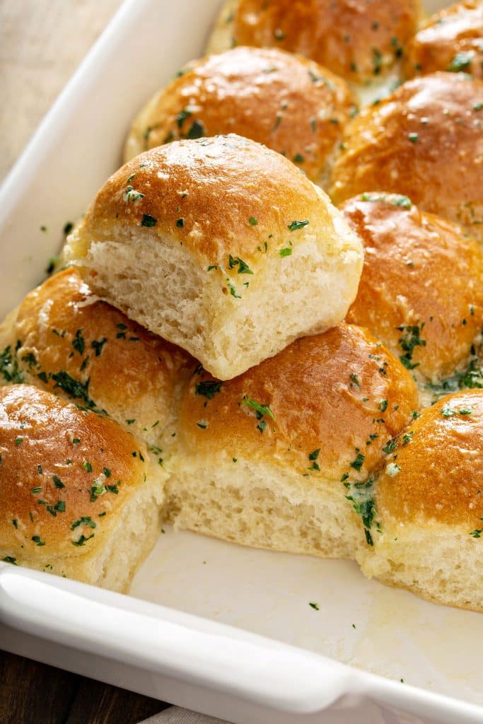 Soft and fluffy dinner rolls brushed with herbed butter on a baking dish.
