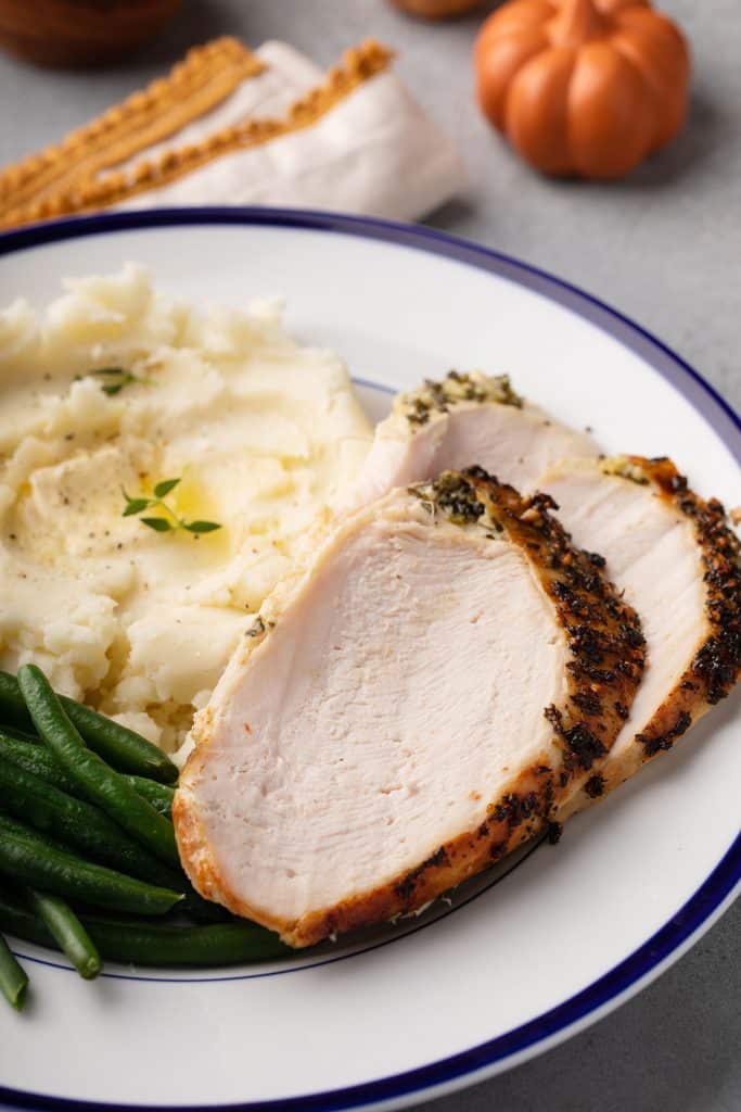 Slices of roasted turkey breast with herbs served with mashed potatoes and green beans.