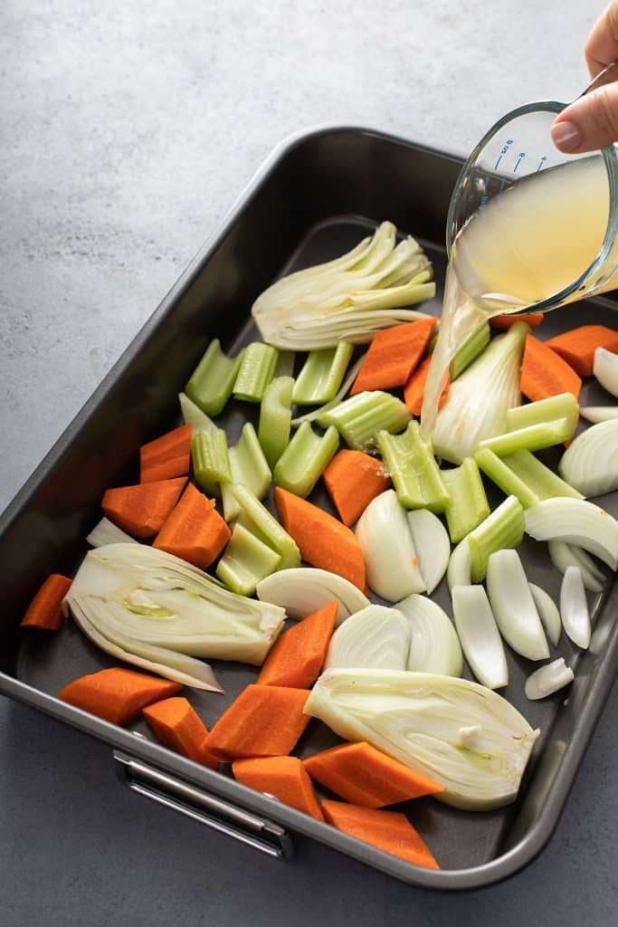 Pouring broth over vegetables in a roasting pan