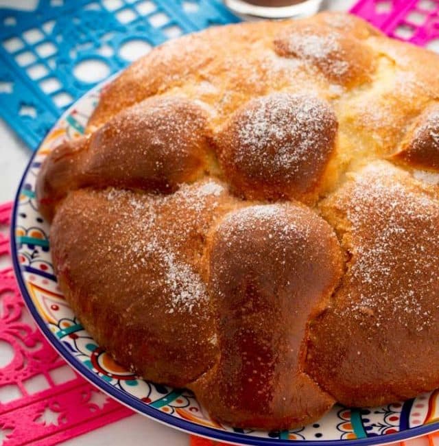 A round loaf of sweet Mexican bread (Pan de Muerto) on a colorful plate.