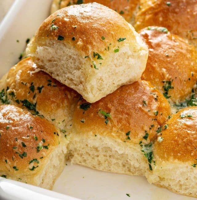 Soft and fluffy dinner rolls brushed with herbed butter on a baking dish.