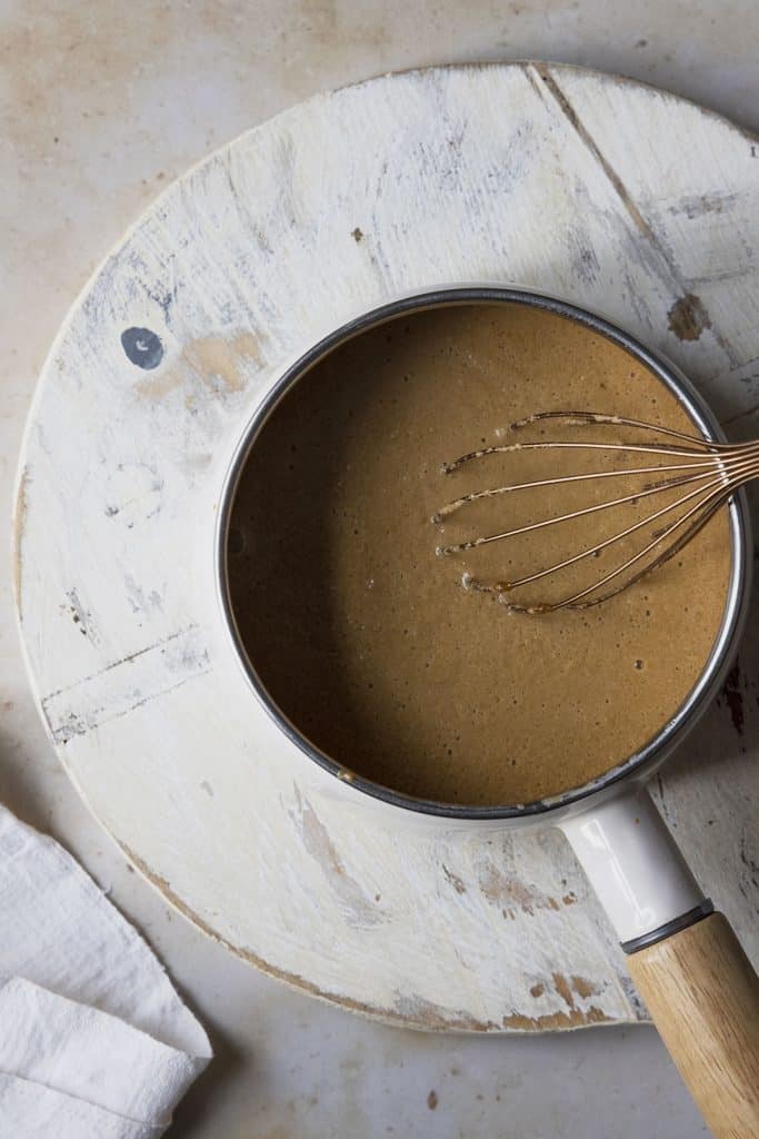 Caramel sauce and milk combined with a whisk in a saucepan.