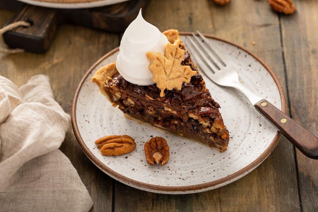 A slice of A piece of Chocolate Pecan pie topped with whipped cream and a leaf made of pie crust.