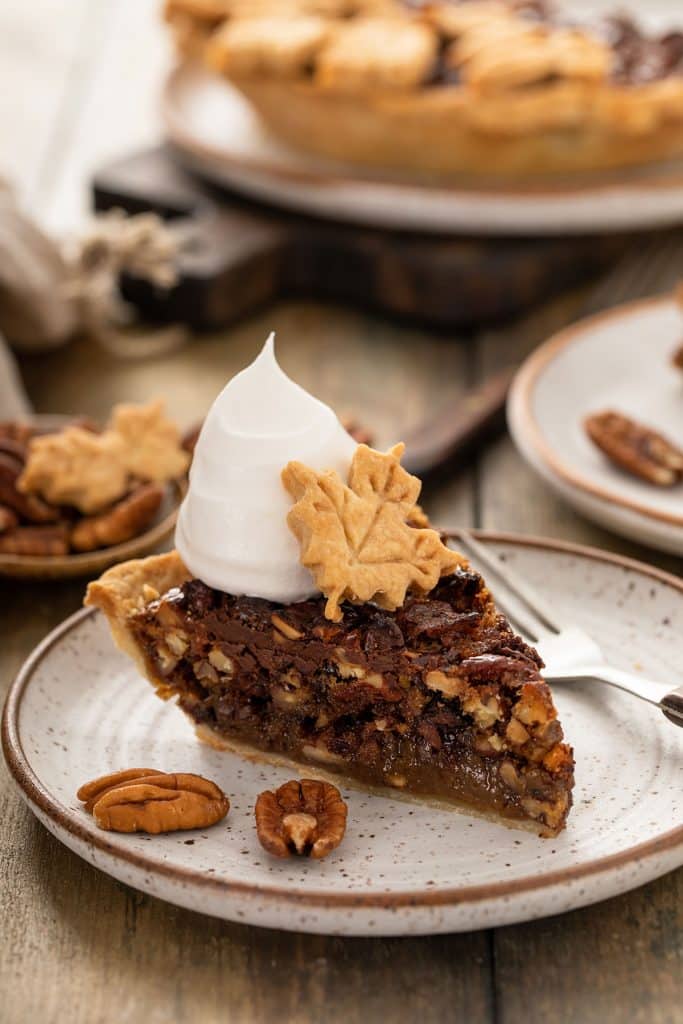 A piece of Chocolate Pecan pie topped with whipped cream and a leaf made of pie crust.