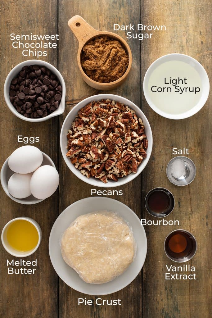 Ingredients to make rich and decadent Chocolate Pecan Pie on a wooden surface.