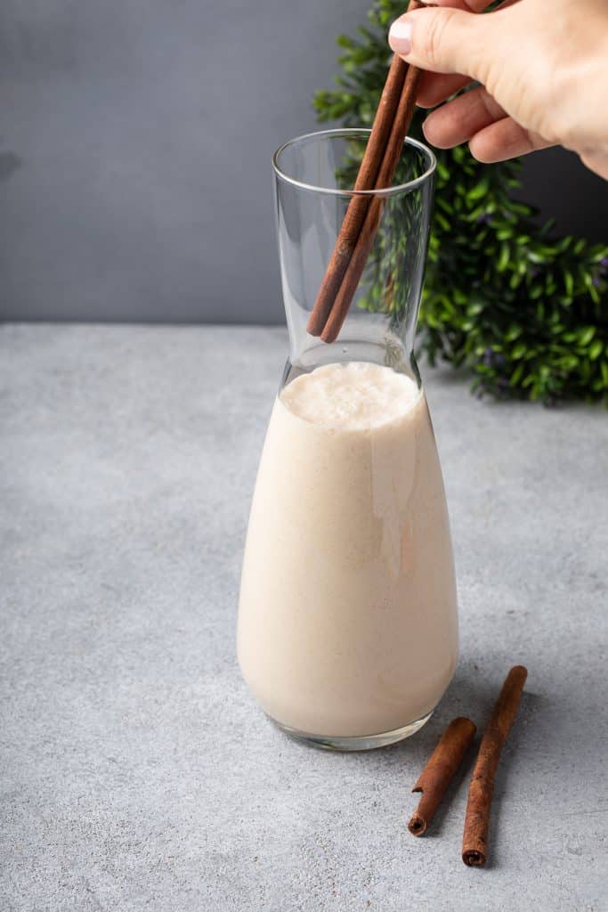 adding cinnamon sticks to Coconut nog aka coquito in a glass bottle