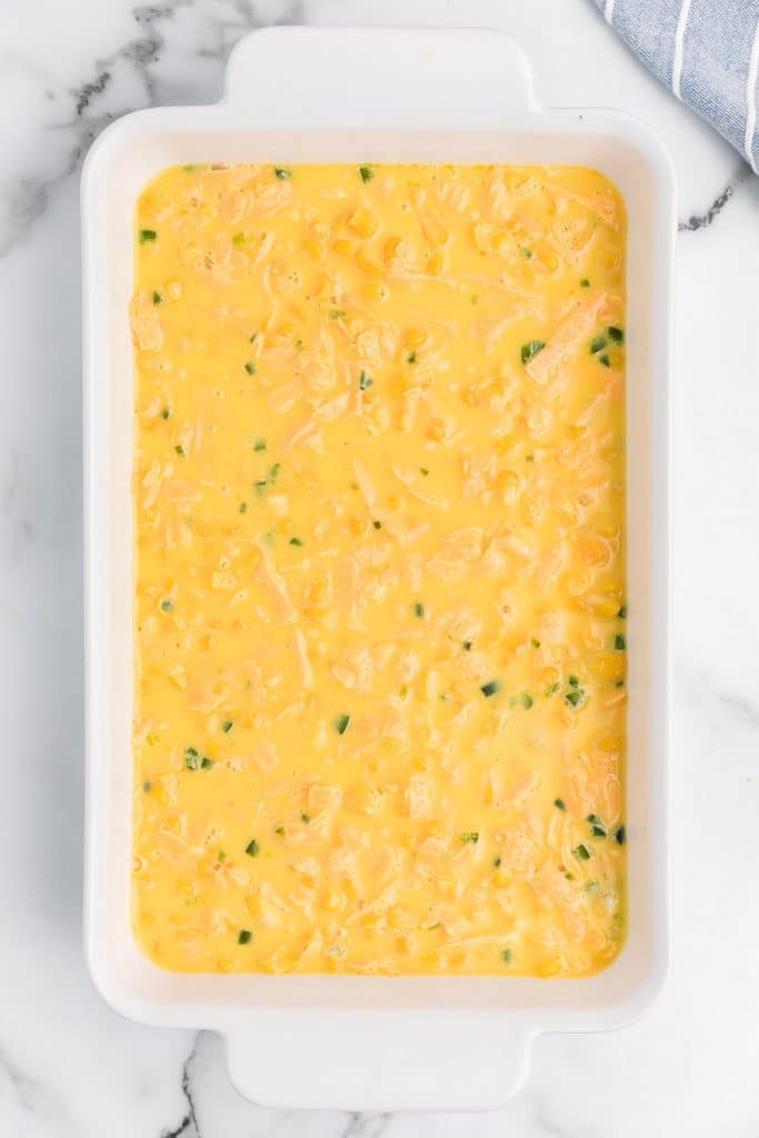 corn pudding mixture in a white baking dish.