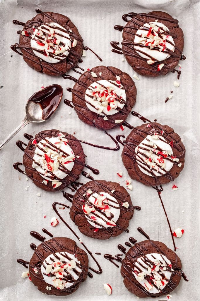 top view of eight hot cocoa cookies topped with marshmallows, crushed peppermint and drizzled with chocolate.