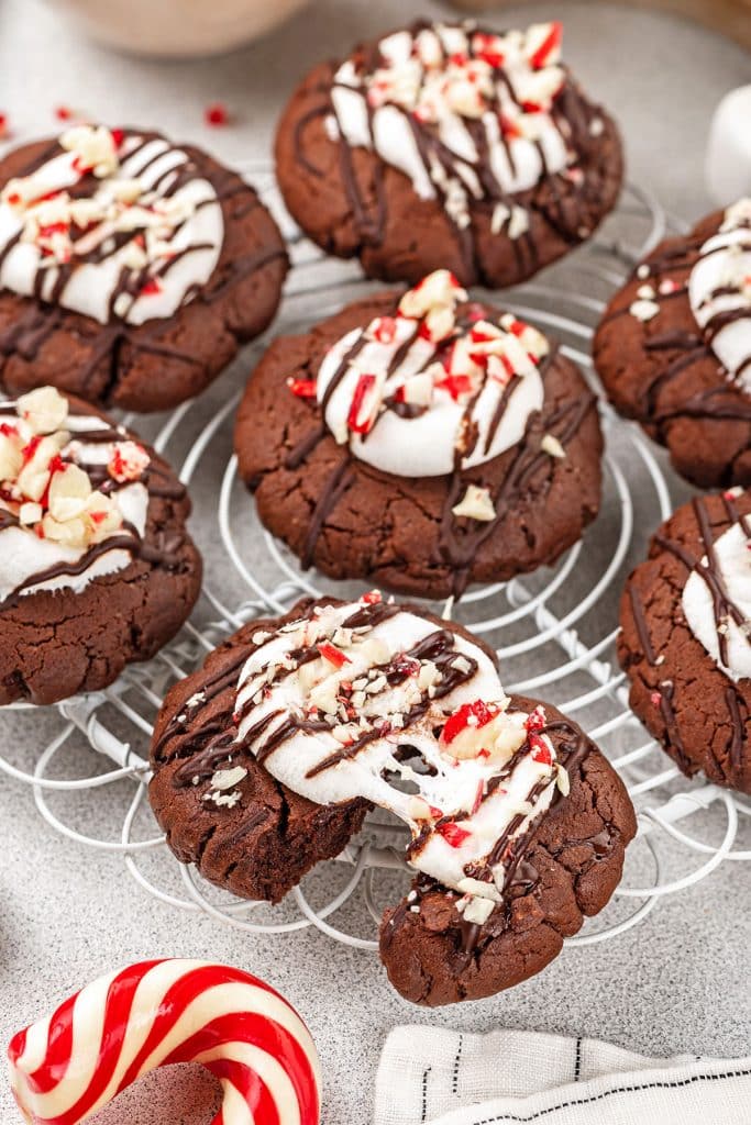 peppermint hot cocoa cookies topped with melted marshmallow and crushed peppermint candy on a white wire rack.