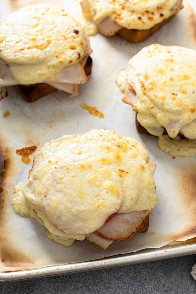 Broiled sandwich with a golden brown cheesy top on a baking sheet pan