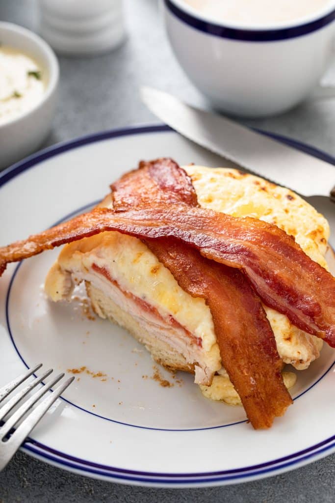 Hot brown turkey sandwich topped with crispy bacon on a plate, cut up
